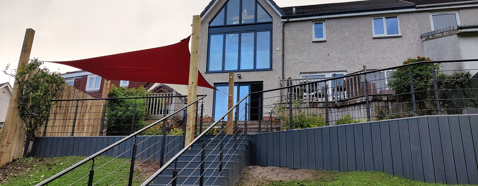 A view of the staircase leading up to the decking, flanked by a modern black balustrade with horizontal wire detailing.